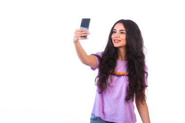 Genç kız beyaz arka planda cep telefonuyla selfie çekiyor. Yüksek kalite fotoğraf