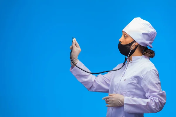 Giovane Infermiera Maschera Nera Controlla Paziente Con Stetoscopio Sfondo Blu — Foto Stock