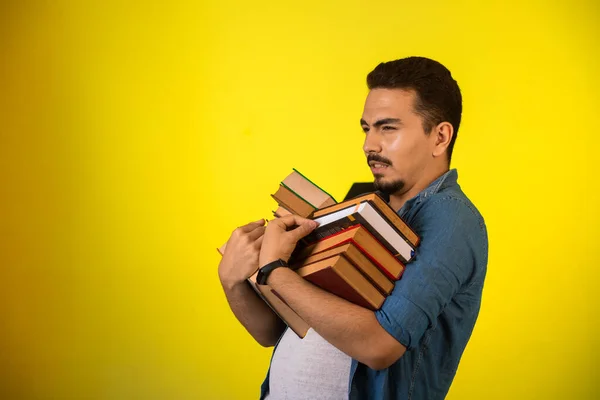 Man carrying a pile of books on yellow background. High quality photo