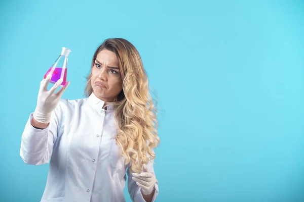 ピンクの液体で化学フラスコを保持白い制服の看護師と疑問に見える 高品質の写真 — ストック写真