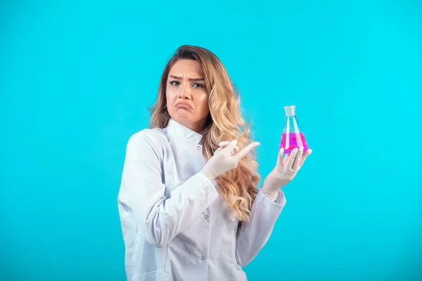 ピンクの液体で化学フラスコを保持し 混乱を感じる白い制服の看護師 高品質の写真 — ストック写真