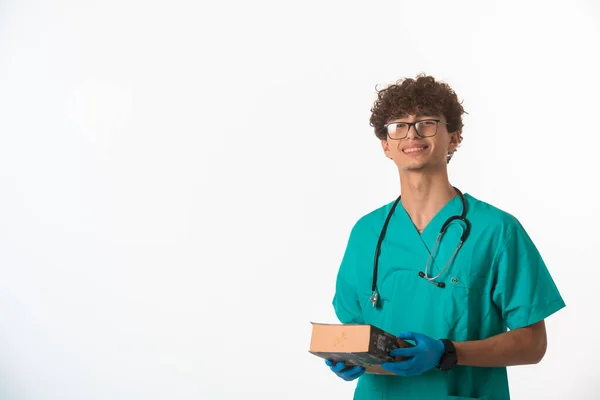 Lockiger Junge Arztuniform Der Ein Großes Buch Beiden Händen Hält — Stockfoto