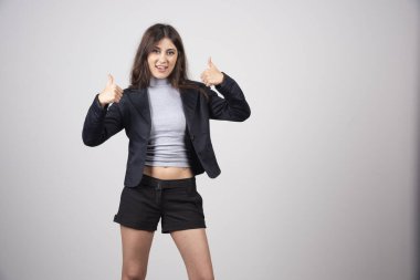 Ceketli genç bir iş kadını gri bir duvarın üzerinde baş parmak gösteriyor. Yüksek kalite fotoğraf