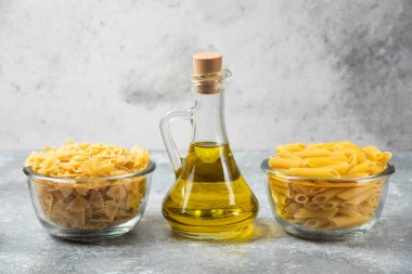 İki kase çiğ makarna ve mermer zemin üzerinde bir şişe zeytin yağı olan farfalle makarna. Yüksek kalite fotoğraf