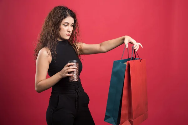 女人拿着杯子 用红色背景展示她的两袋新衣服 — 图库照片