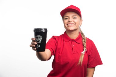 Kırmızı üniformalı gülümseyen kadın beyaz arka planda bir fincan kahve tutuyor. 