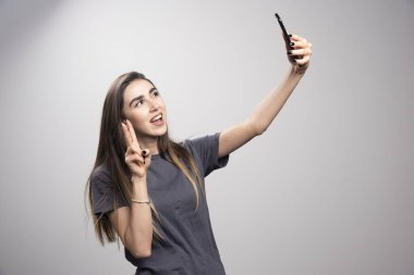 Gri kazaklı, gülümseyen genç bir kadın resmi cep telefonuyla selfie çekiyor. Yüksek kalite fotoğraf