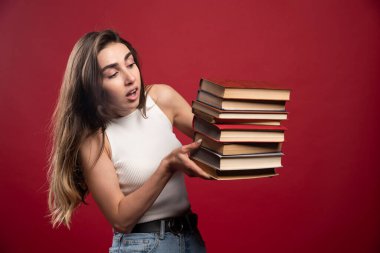 Kırmızı arka planda bir sürü kitap taşıyan genç ve güzel bir kadın model. Yüksek kalite fotoğraf