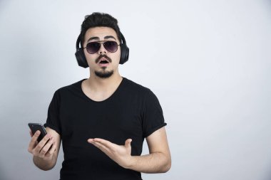 Güneş gözlüklü, kulaklıklı, elinde cep telefonu olan esmer bir adam. Yüksek kalite fotoğraf