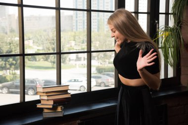 Pencerenin yanında kitaplarla poz veren şaşırmış kadın.