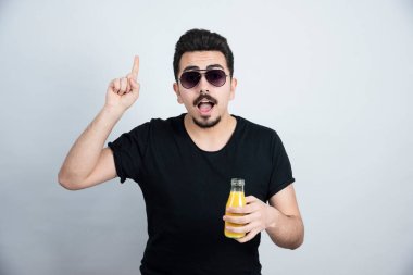 Güneş gözlüklü yakışıklı modelin elinde portakal suyu şişesiyle fotoğrafı. Yüksek kalite fotoğraf