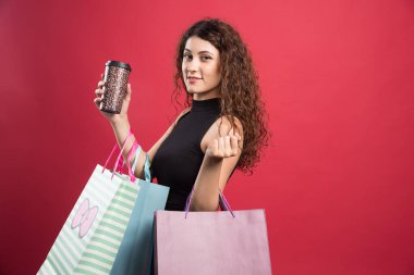 Bardaklı kadın kırmızı arka planda alışverişlerini gösteriyor. 