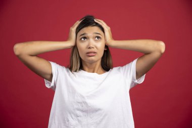 Genç bir kadın kırmızı arka planda kafasına dokunuyor. Yüksek kaliteli fotoğraf.