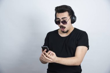 Güneş gözlüklü, kulaklıklı, elinde cep telefonu olan esmer bir adam. Yüksek kalite fotoğraf