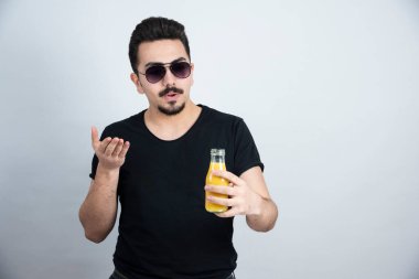 Güneş gözlüklü yakışıklı modelin elinde portakal suyu şişesiyle fotoğrafı. Yüksek kalite fotoğraf