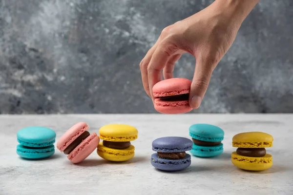 Mano Mujer Sosteniendo Macaron Rosa Sobre Mesa Blanca Con Docenas — Foto de Stock