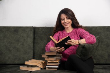 Kanepede kitap yığınıyla kitap okuyan gülümseyen kız. Yüksek kalite fotoğraf