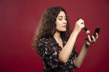 Kırmızı arka planda fırçayla bronzlaştırıcı süren zarif bir kadın. Yüksek kalite fotoğraf