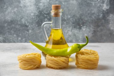 Pişmemiş makarna yuvaları, bir şişe zeytinyağı ve beyaz masada yeşil biber. Yüksek kalite fotoğraf