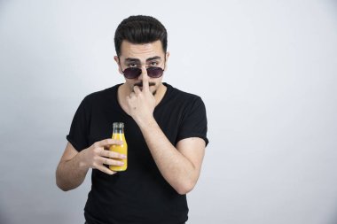 Güneş gözlüklü yakışıklı modelin elinde portakal suyu şişesiyle fotoğrafı. Yüksek kalite fotoğraf