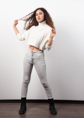 Beyaz bir duvarın üzerinde duran beyaz kazaklı genç bir kadın. Yüksek kalite fotoğraf