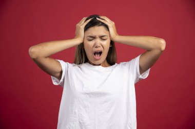 Genç bir kadın kırmızı arka planda kafasına dokunuyor. Yüksek kaliteli fotoğraf.