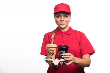 Kırmızı üniformalı kadın elinde beyaz arka planda iki fincan kahve tutuyor. 