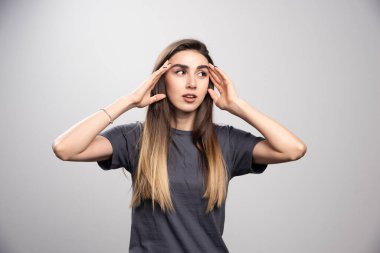 Gri arka planda başını okşayan genç bir kadının portresi. Yüksek kalite fotoğraf