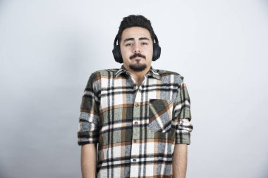 Beyaz duvarın üzerinden kameraya bakan kulaklıklı yakışıklı bir adam resmi. Yüksek kalite fotoğraf