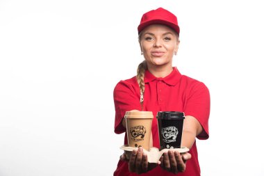Kırmızı üniformalı kadın elinde beyaz arka planda iki fincan kahve tutuyor. 