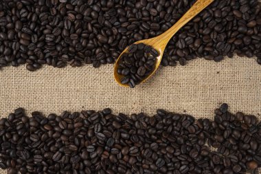 Çuval bezine saçılmış ahşap kaşıklı orta pişmiş kahve çekirdeği yığını. Yüksek kalite fotoğraf