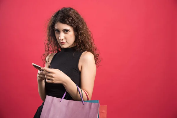 Vrouw Glimlachend Met Tassen Van Nieuwe Kleren Telefoon Rode Achtergrond — Stockfoto