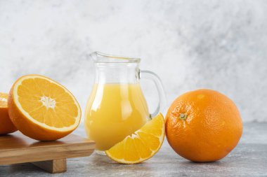 Taş zemin üzerinde taze portakal meyveleri olan cam bir sürahi meyve suyu. Yüksek kalite fotoğraf