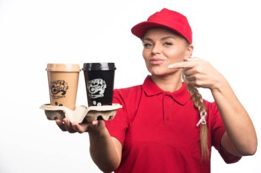 Kırmızı üniformalı kadın beyaz arka planda kahveli bardakları işaret ediyor. 