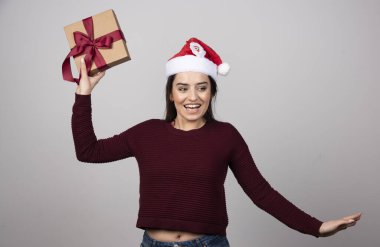Noel Baba şapkalı gülümseyen kız gri arka planda hediye kutusuyla dans ediyor. Yüksek kalite fotoğraf