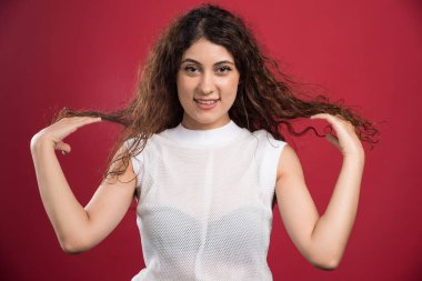 Güzel bir kadın kırmızı arka planda kıvırcık siyah saçlarına dokunuyor. Yüksek kalite fotoğraf