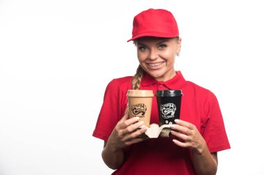 Kırmızı üniformalı kadın elinde beyaz arka planda iki fincan kahve tutuyor. 