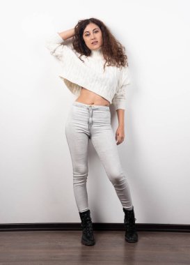 Beyaz bir duvarın üzerinde duran beyaz kazaklı genç bir kadın. Yüksek kalite fotoğraf