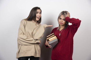 Bir kız bir yığın kitap tutuyor, diğeri de ona gösteriyor. Yüksek kalite fotoğraf