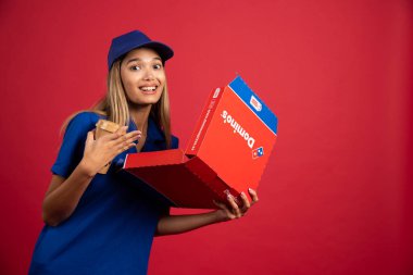 Mavi üniformalı bir kadın kurye elinde bir fincan ve açılmış bir pizza kutusu tutuyor. Yüksek kalite fotoğraf