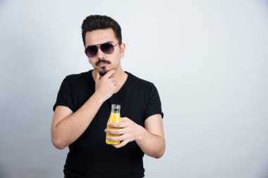 Güneş gözlüklü yakışıklı modelin elinde portakal suyu şişesiyle fotoğrafı. Yüksek kalite fotoğraf