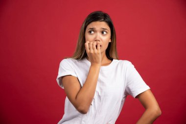 Genç bir kadın kırmızı arka planda yüzüne dokunuyor.