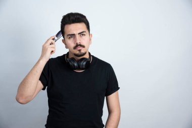 Esmer adam, kulaklıkla durup beyaz duvara karşı poz veriyor. Yüksek kalite fotoğraf