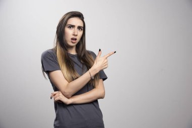 Gri bir arkaplan üzerinde ayakta duran ve işaret eden kadın portresi. Yüksek kalite fotoğraf