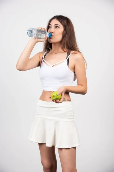 若いブルネットの女性はリンゴ飲料水とスポーツウェアを着ています 高品質の写真 — ストック写真