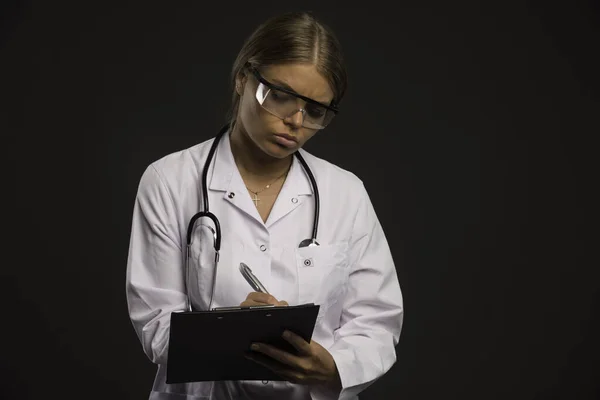 眼鏡をかけた聴診器を装着した金髪女医師が患者に領収書を書きます 高品質の写真 — ストック写真