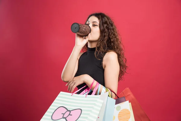 Vrouw Drinkend Uit Beker Met Tassen Rode Achtergrond Hoge Kwaliteit — Stockfoto