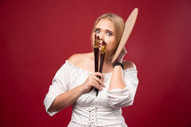 Sarışın sanatçı palet ve fırça tutuyor ve şaşırmış ve kafası karışmış görünüyor. Yüksek kalite fotoğraf