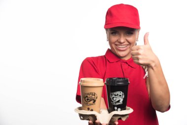 Kırmızı üniformalı kadın elinde beyaz arka planda iki fincan kahve tutuyor. 