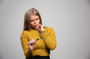 Sarışın kız bir büyüteç tutuyor ve şüpheli bir şekilde bakıyor. Yüksek kalite fotoğraf